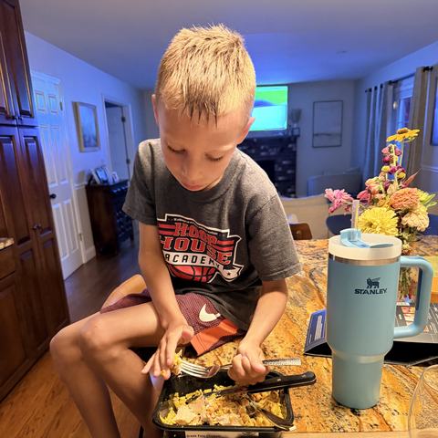 A boy mid-bite of a Strong Kitchen Greek Feta Chicken meal